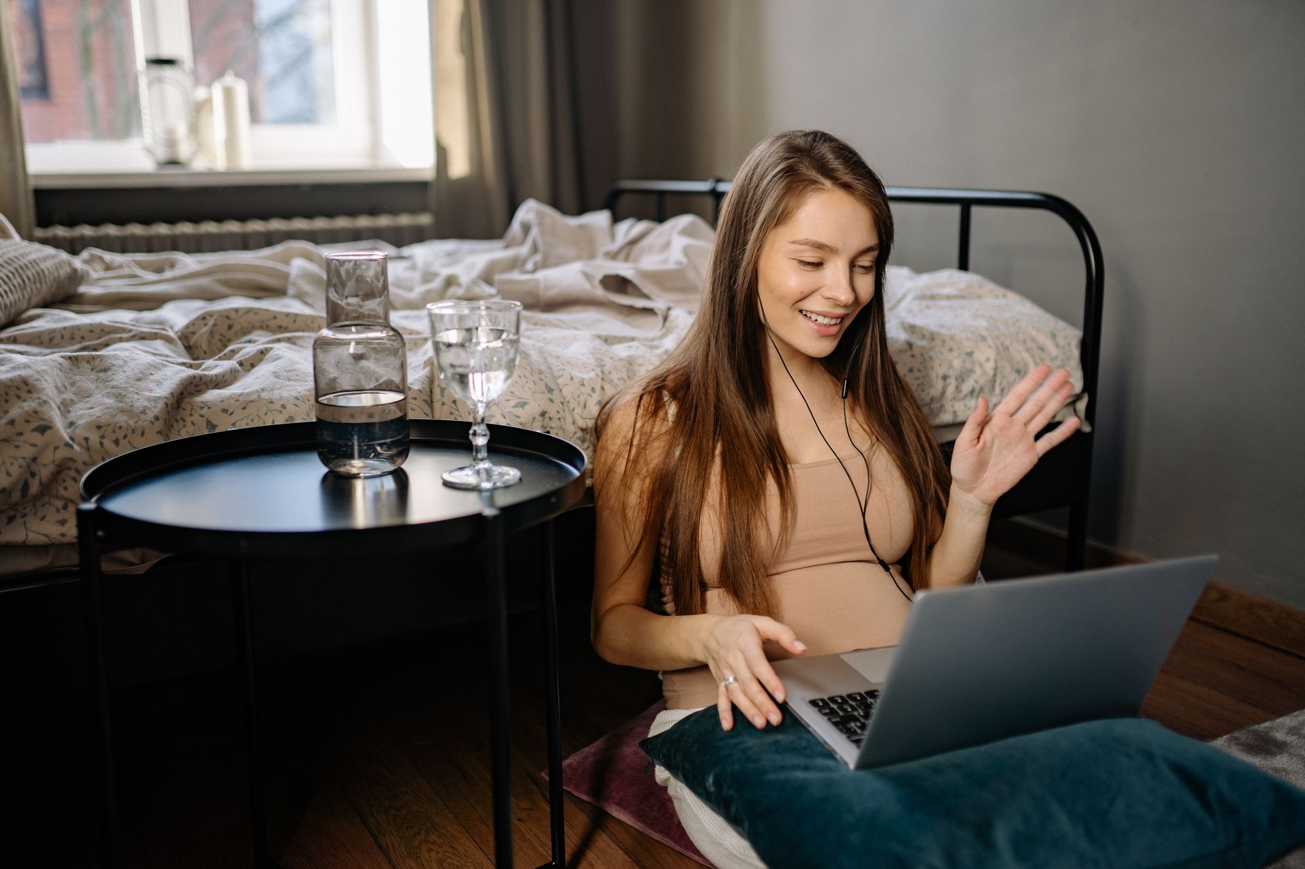 Smiling woman works remotely on laptop while sitting on the floor. A cozy indoor setting ideal for digital nomads.