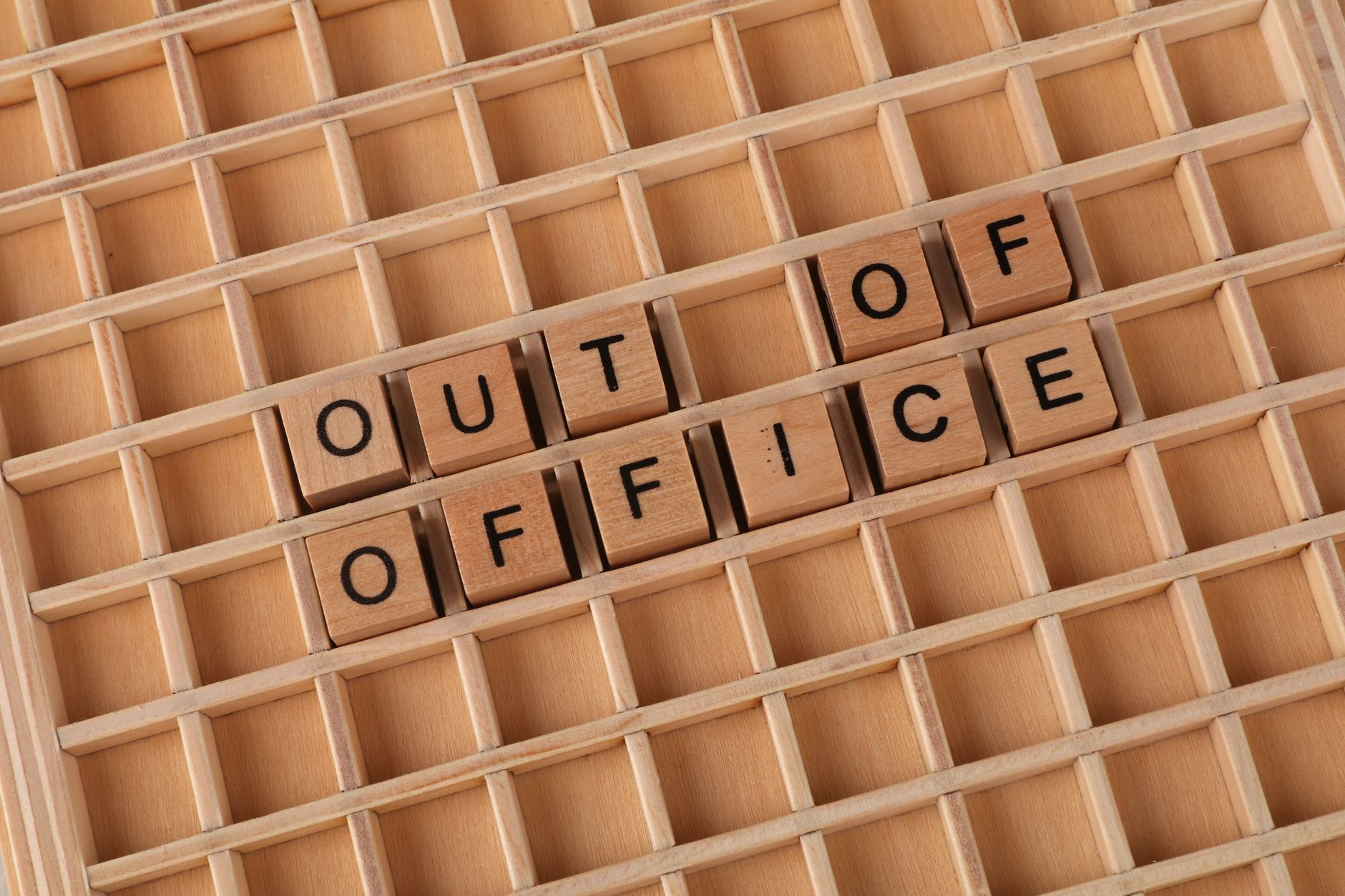 Close-up of wooden letter tiles spelling 'Out of Office' on grid layout background.