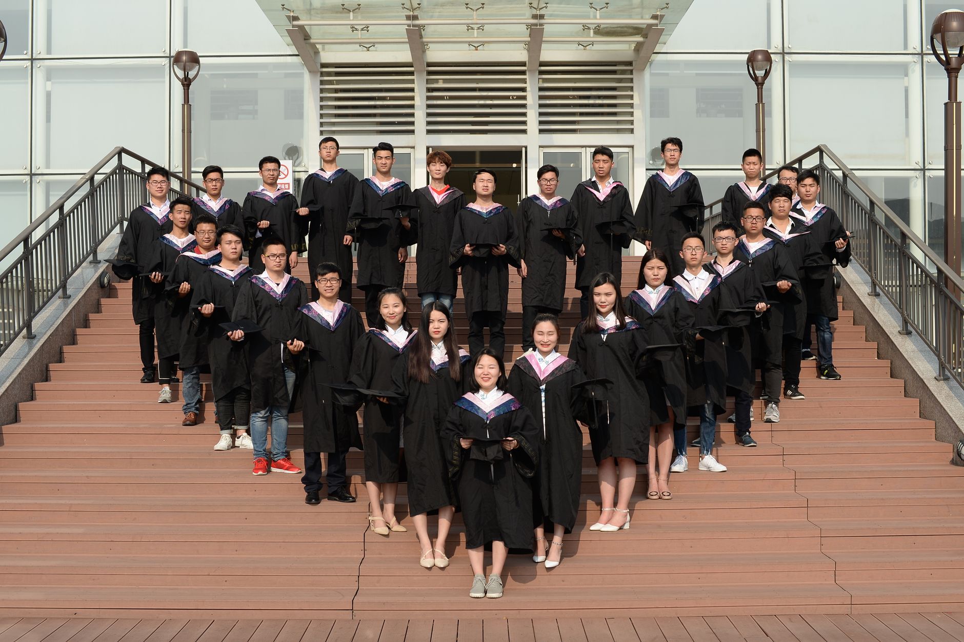 Large group of graduates in caps and gowns posing on campus stairs, celebrating academic achievement.