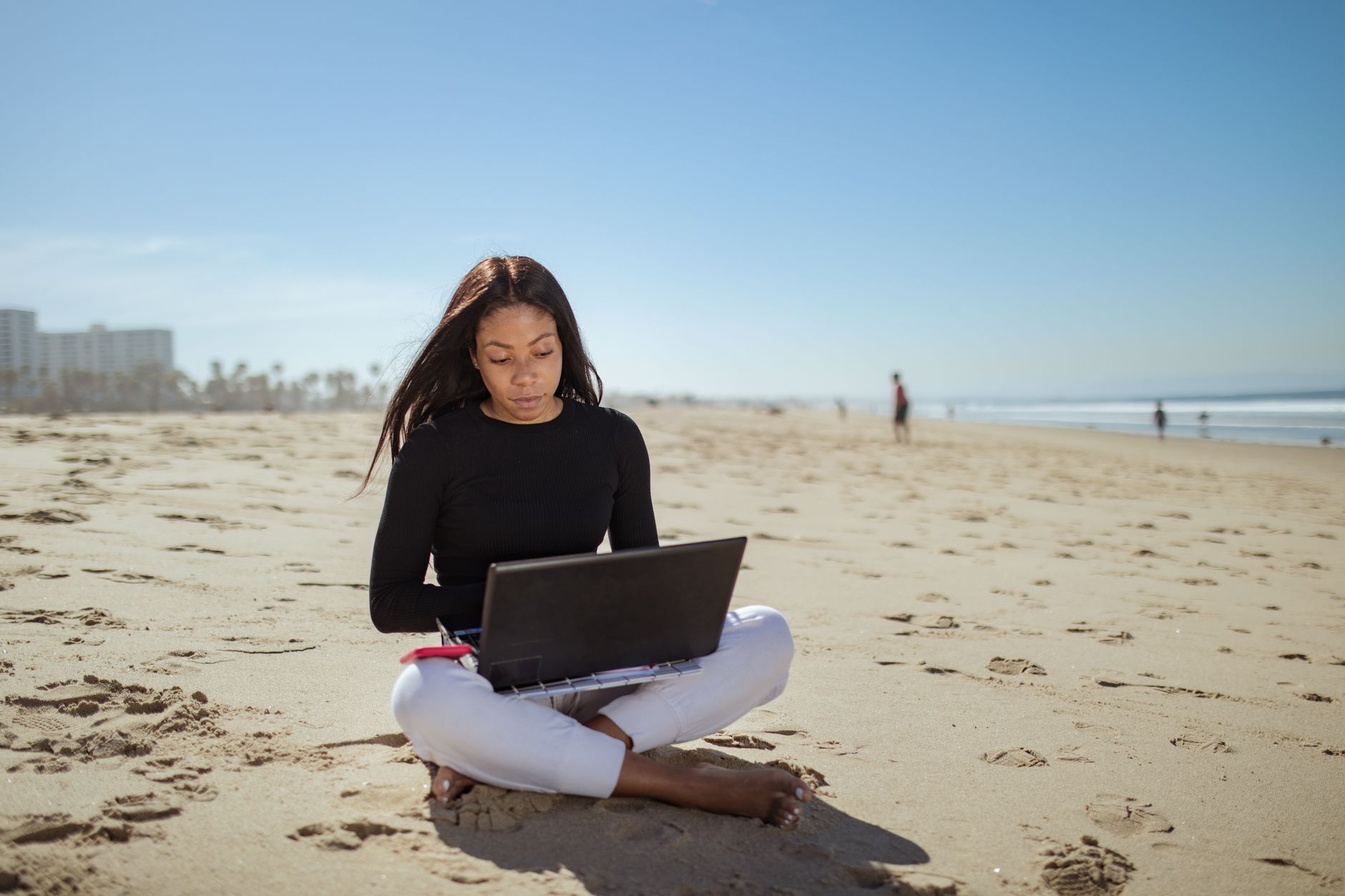 Young woman working remotely on a beach with her laptop, embracing the digital nomad lifestyle.