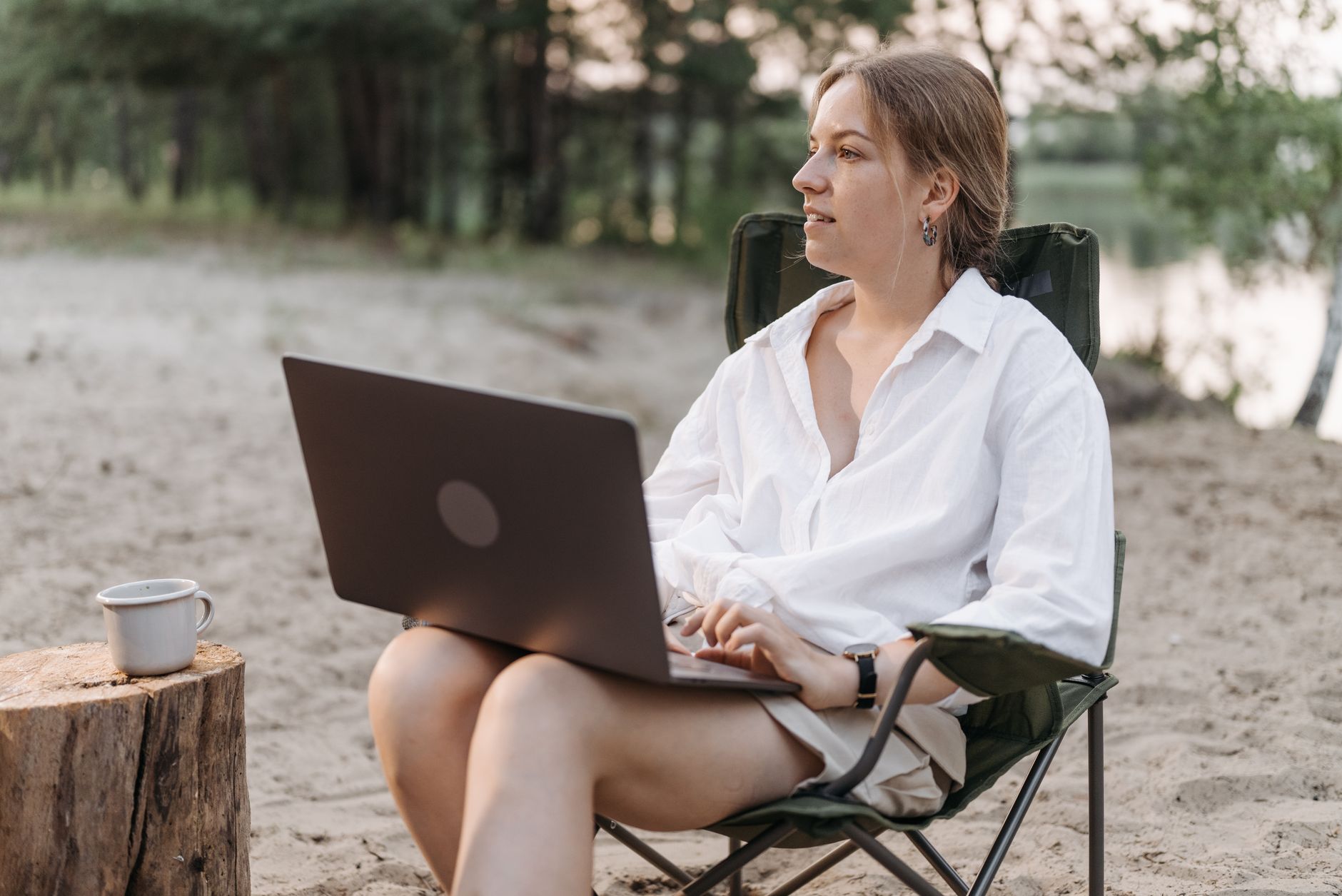 Woman working on a laptop by the beach, highlighting remote work and digital nomad lifestyle.