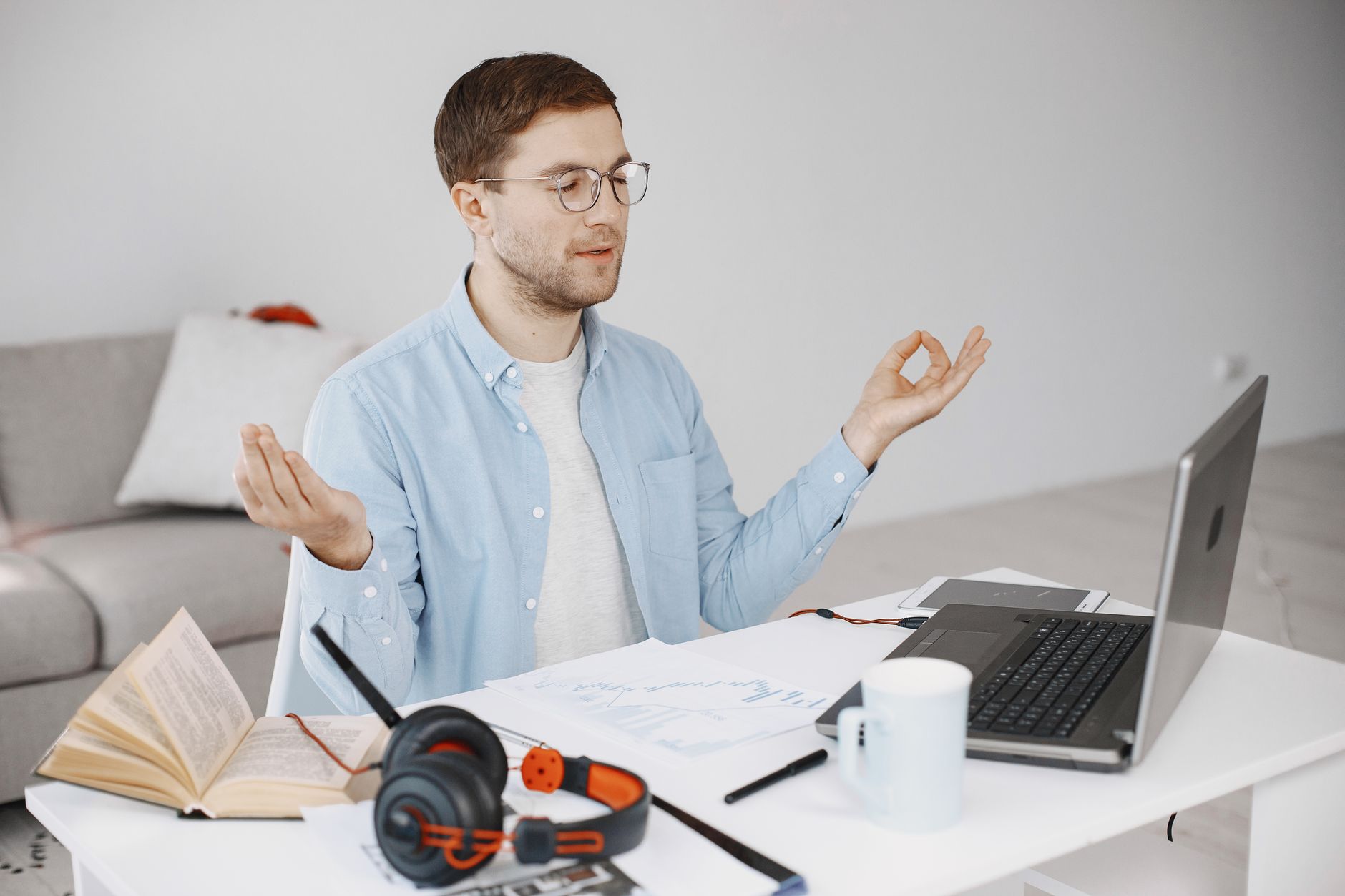 Man practicing meditation at a tidy desk with a laptop, books, and headphones in a home office.