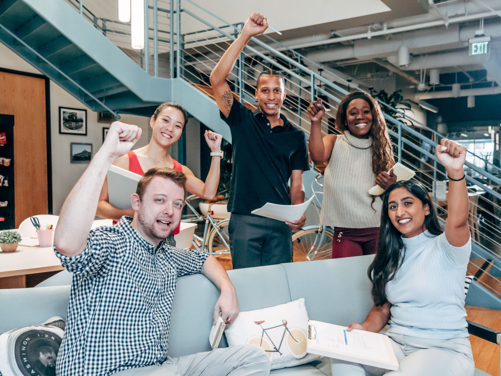 A diverse group of coworkers cheerfully celebrating success in a modern office setting.