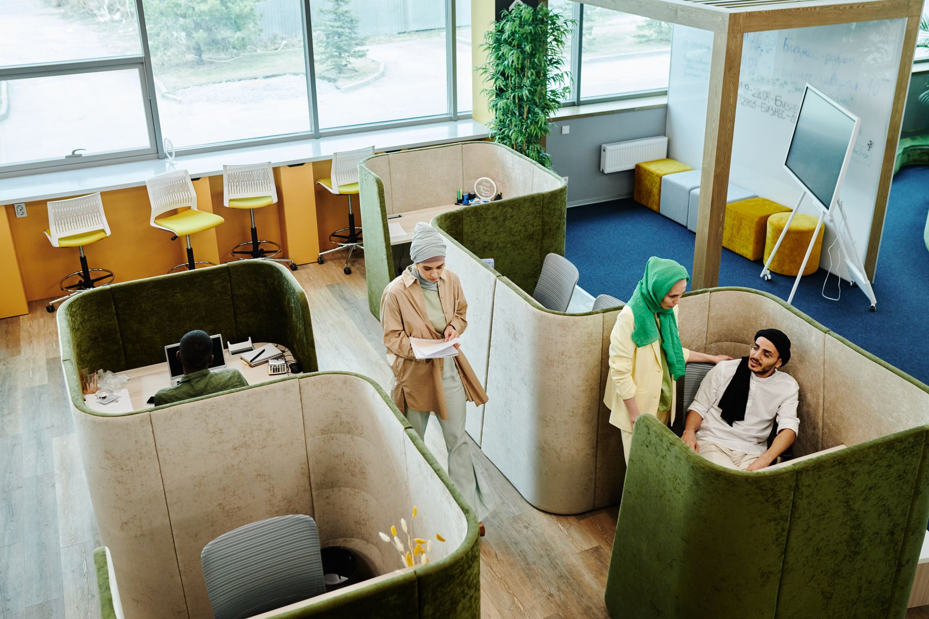 Modern office environment with diverse team collaborating in pod-style workspaces.