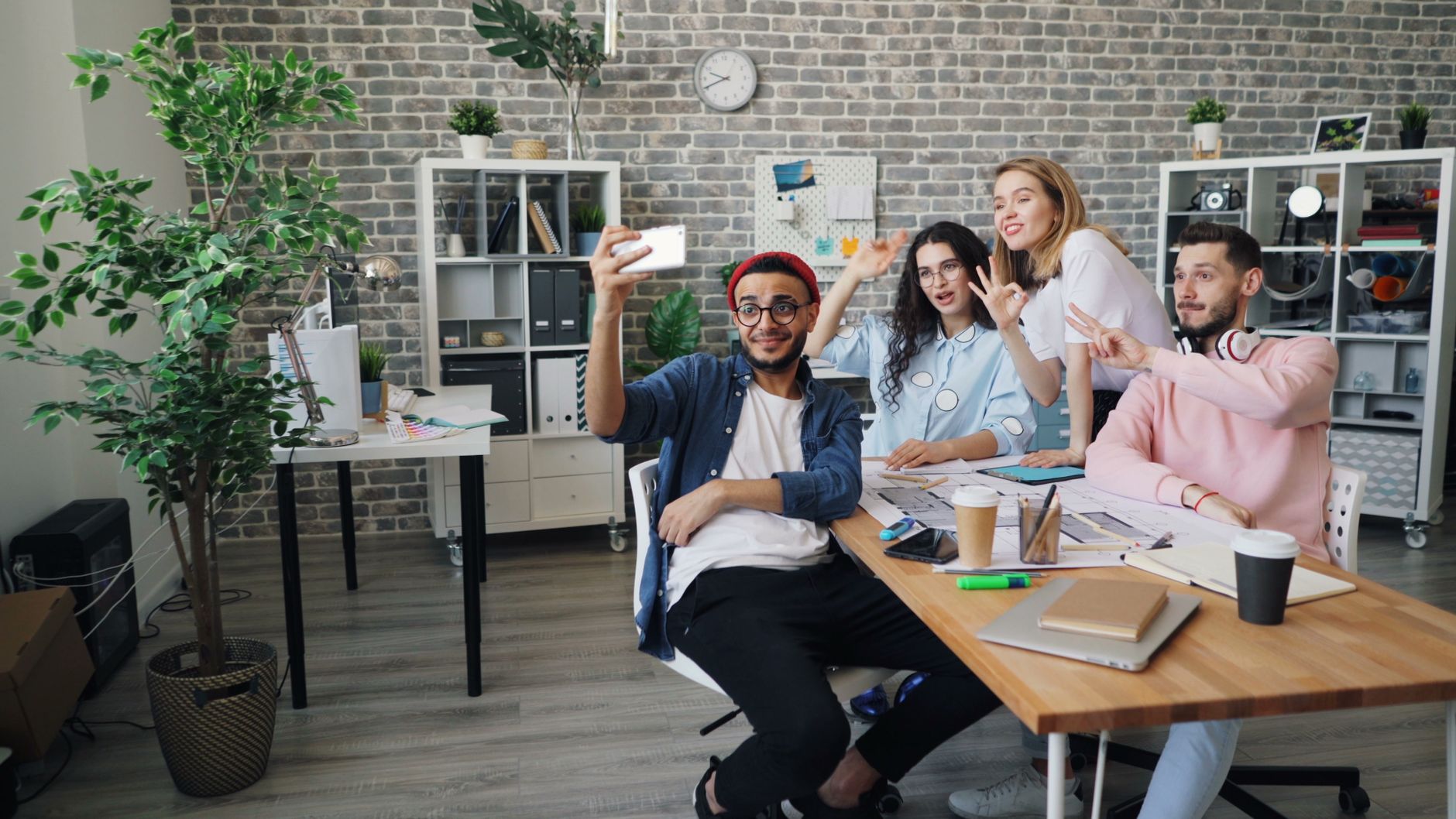 Diverse group of happy young professionals taking a selfie at work, showcasing teamwork and modern office vibes.