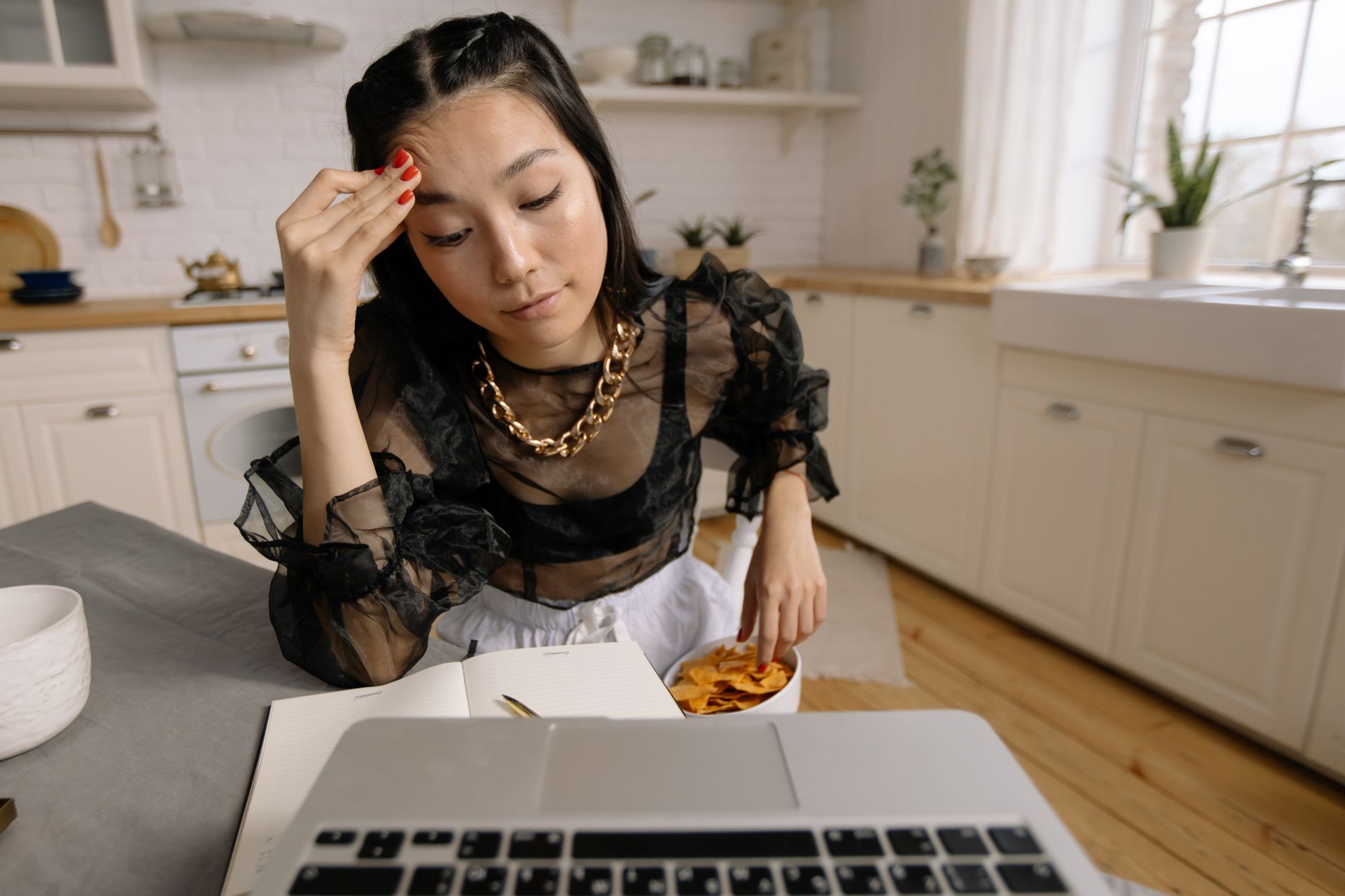 An exhausted woman working from home with a laptop and snacks, depicting remote work life.