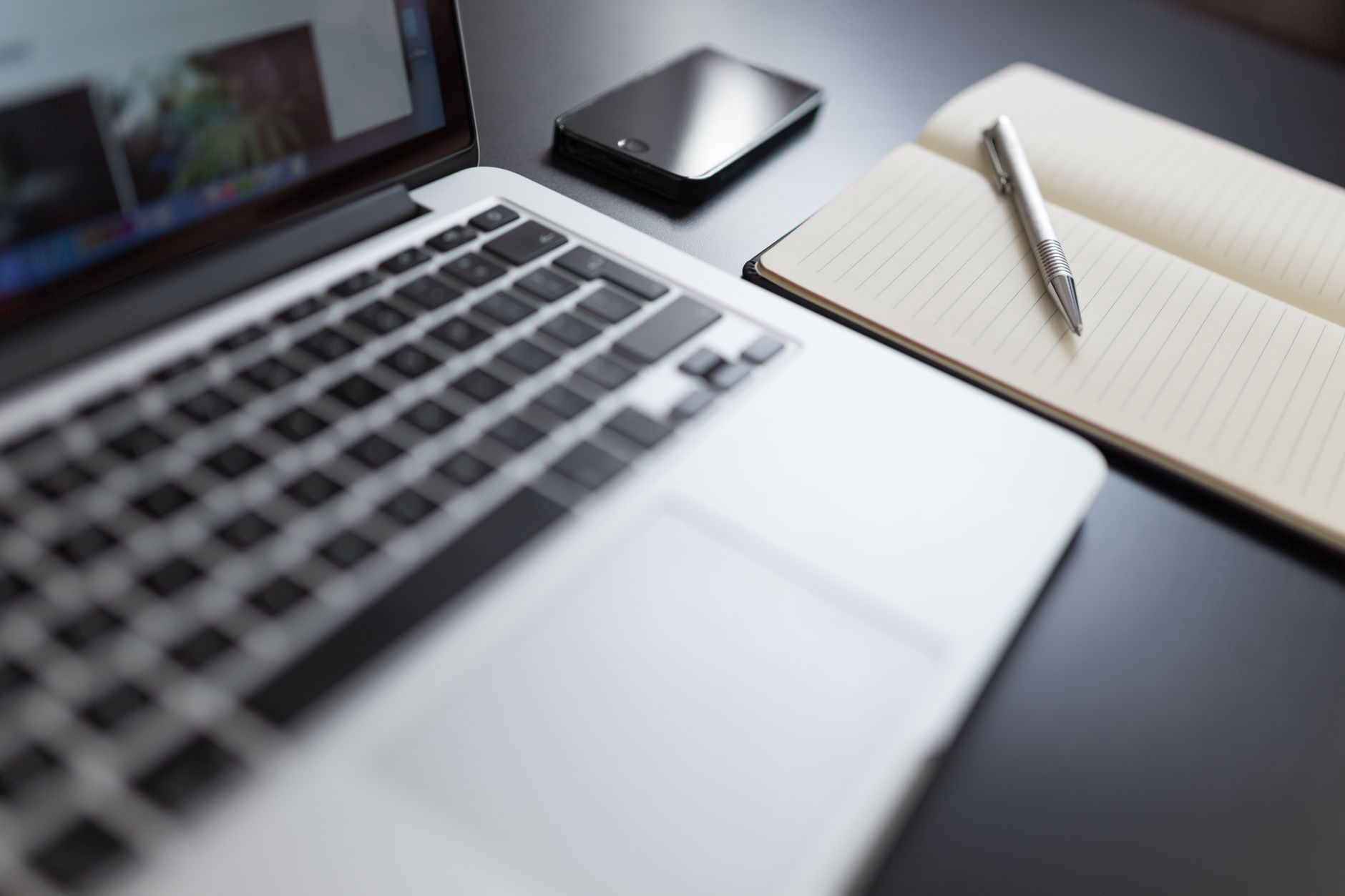 A modern workspace featuring a laptop, notebook, smartphone, and pen on a desk.