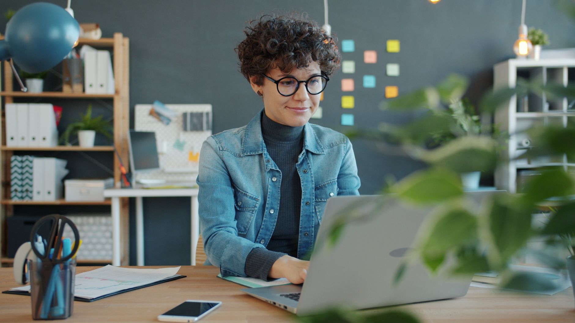 Smiling woman working on laptop in a creative home office space.