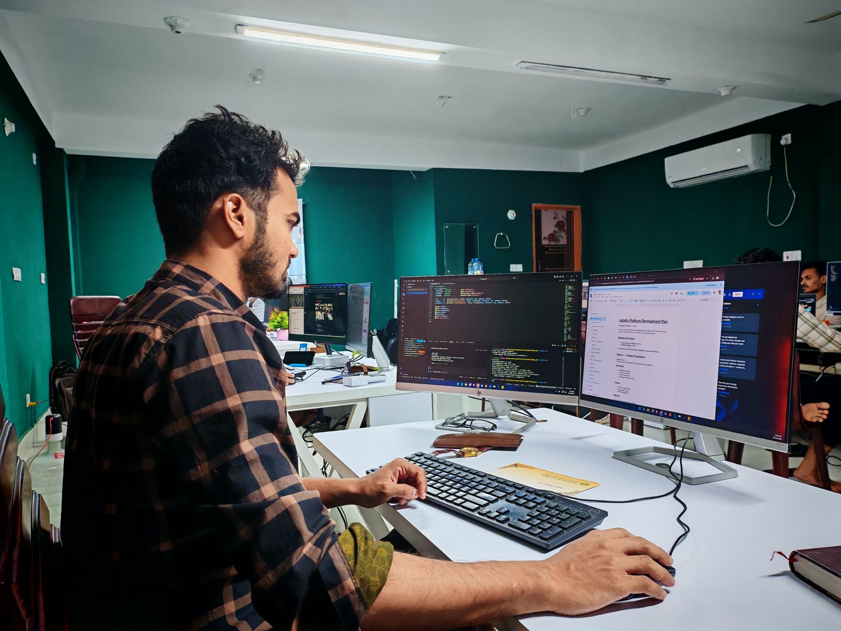 Software developer coding on dual monitors in a well-lit modern office, focused and engaged.