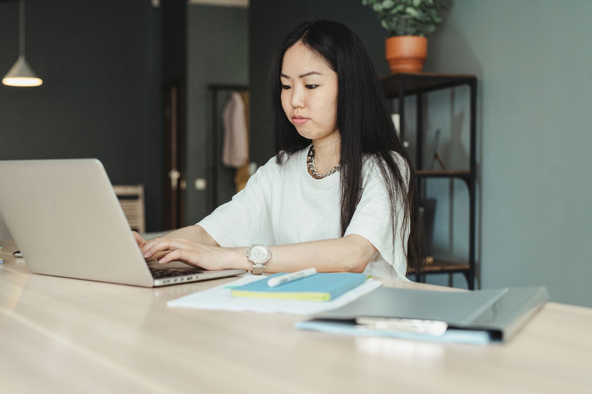 Asian woman freelancer working on a laptop in a modern home office setting. Ideal for workspace, lifestyle, and remote work themes.