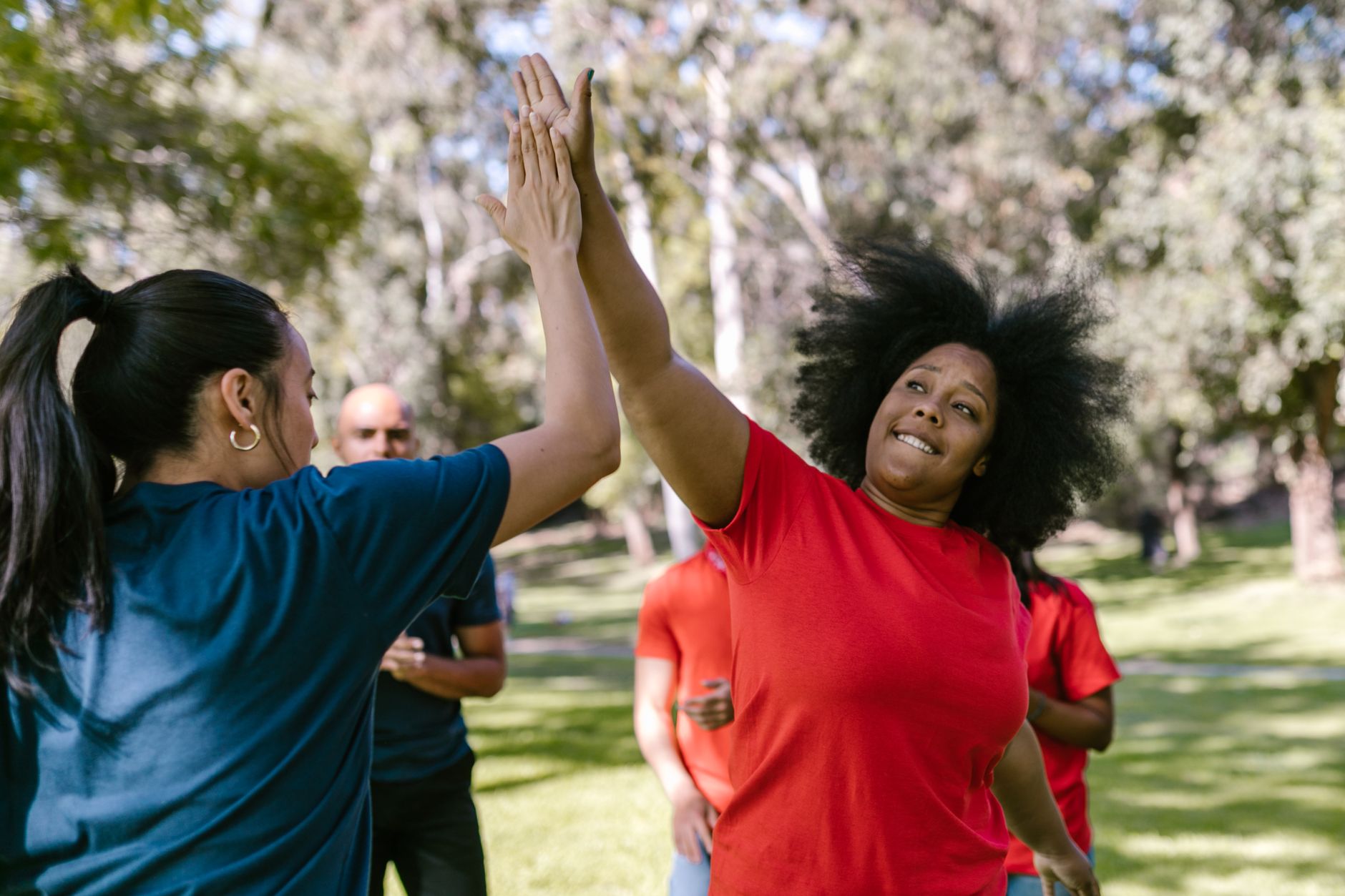 A diverse group celebrates with a high five during an outdoor team-building event.