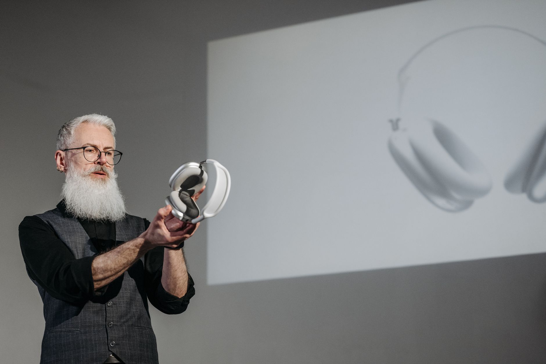 A bearded man presenting a pair of wireless headphones during a business meeting.