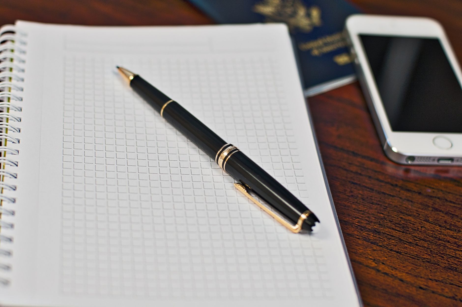 Black pen on a grid notebook with smartphone and passport on wooden desk.