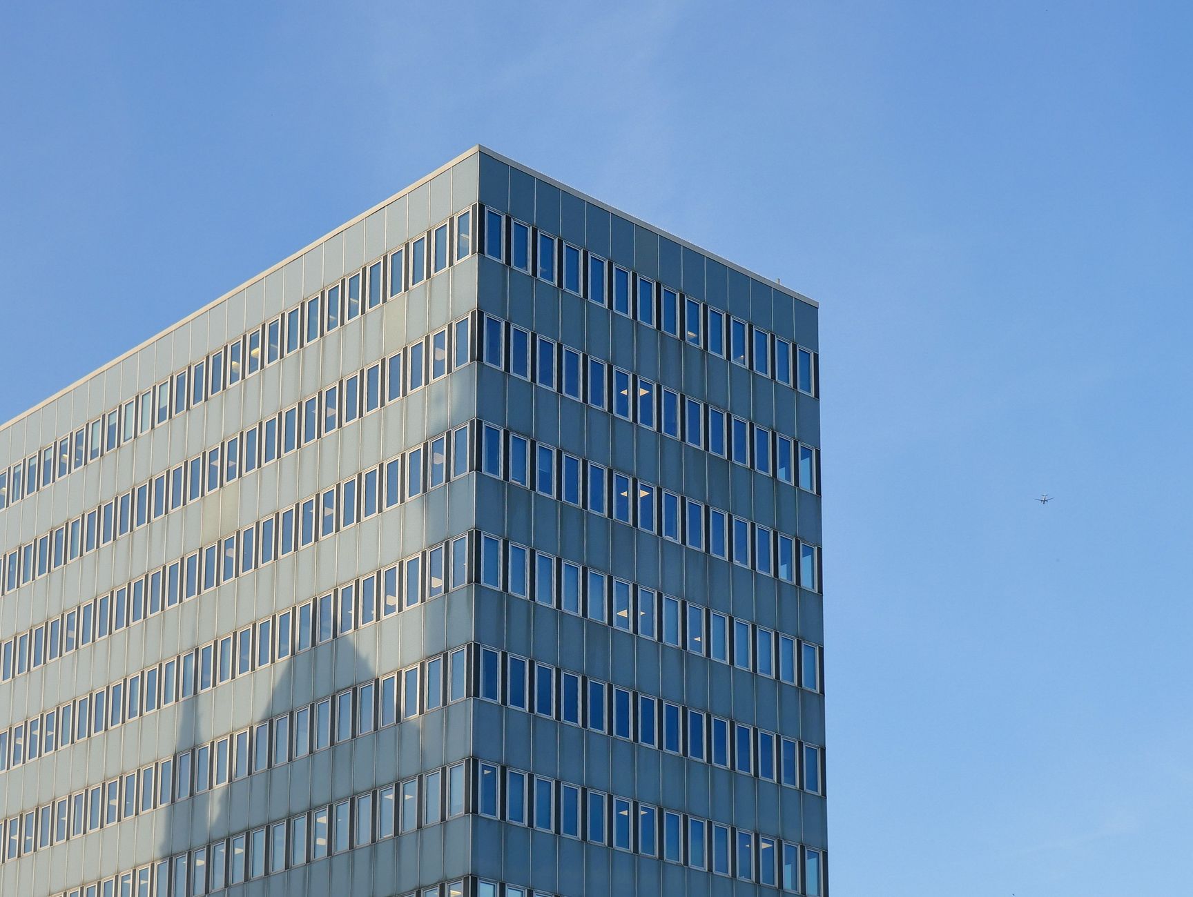 Low angle view of a modern office building facade with glass windows under a clear blue sky.