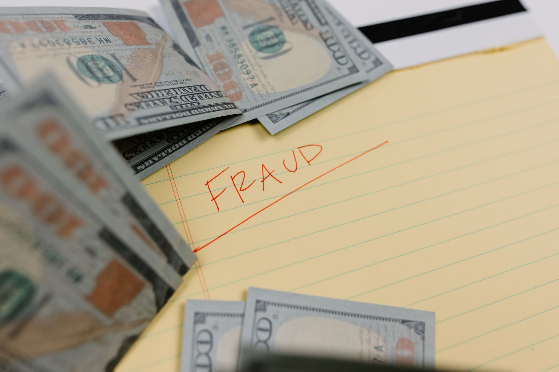 Close-up of US dollars and 'Fraud' written on yellow paper, representing financial scams.