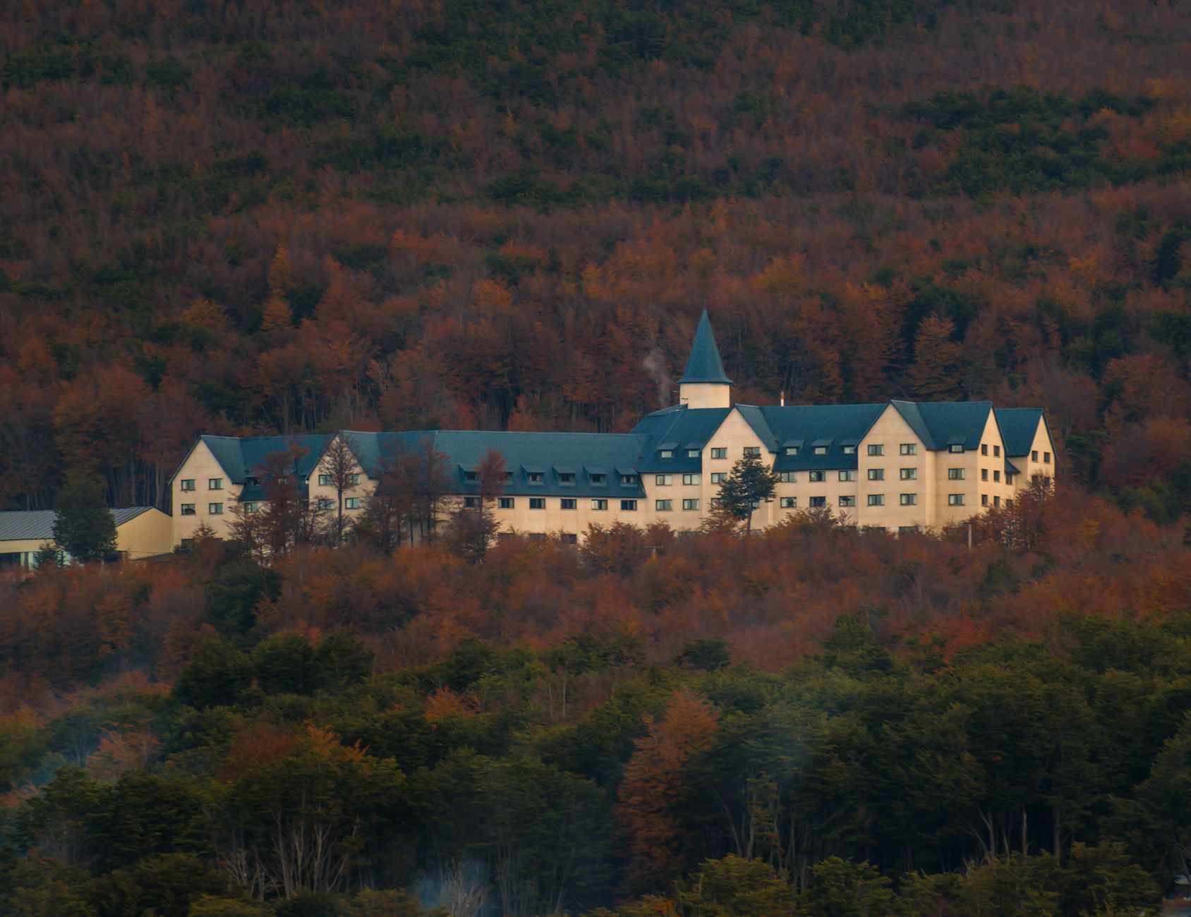 A picturesque hotel surrounded by beautiful autumn foliage set in a mountainous landscape.